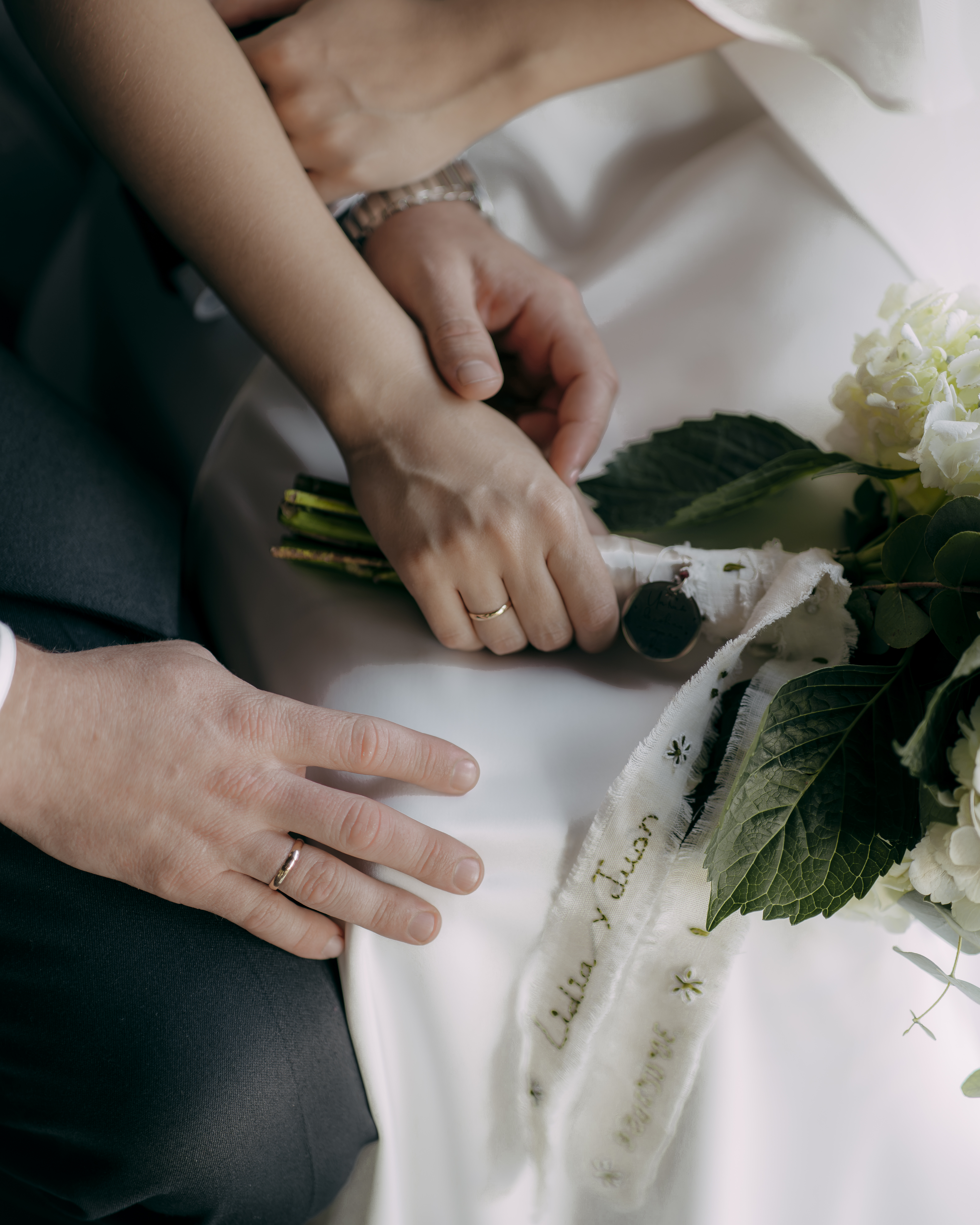 Primer plano de las manos de los novios con los anillos y el ramo