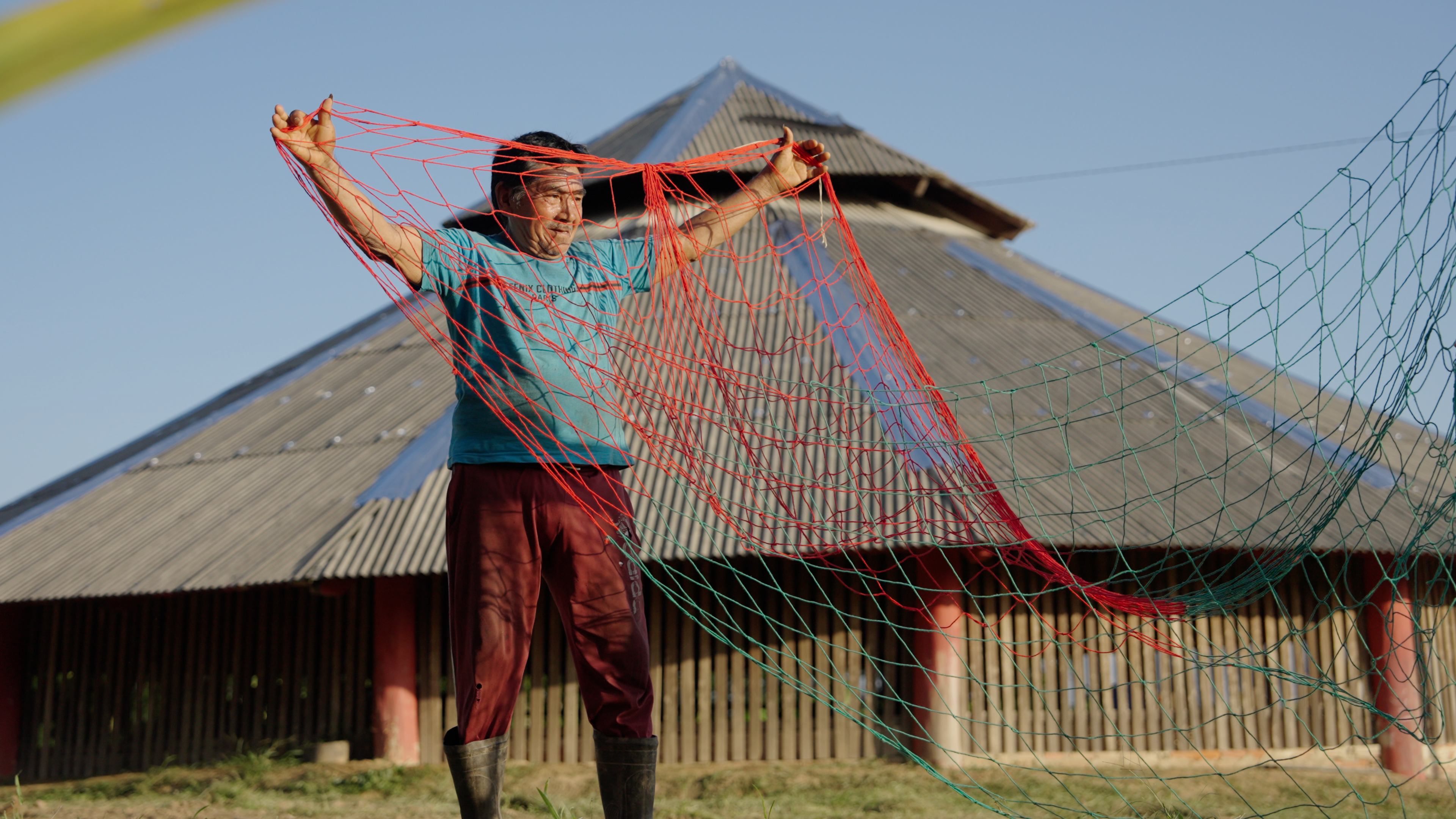 Indigenous man holding a fishing net in front of a traditional communal house