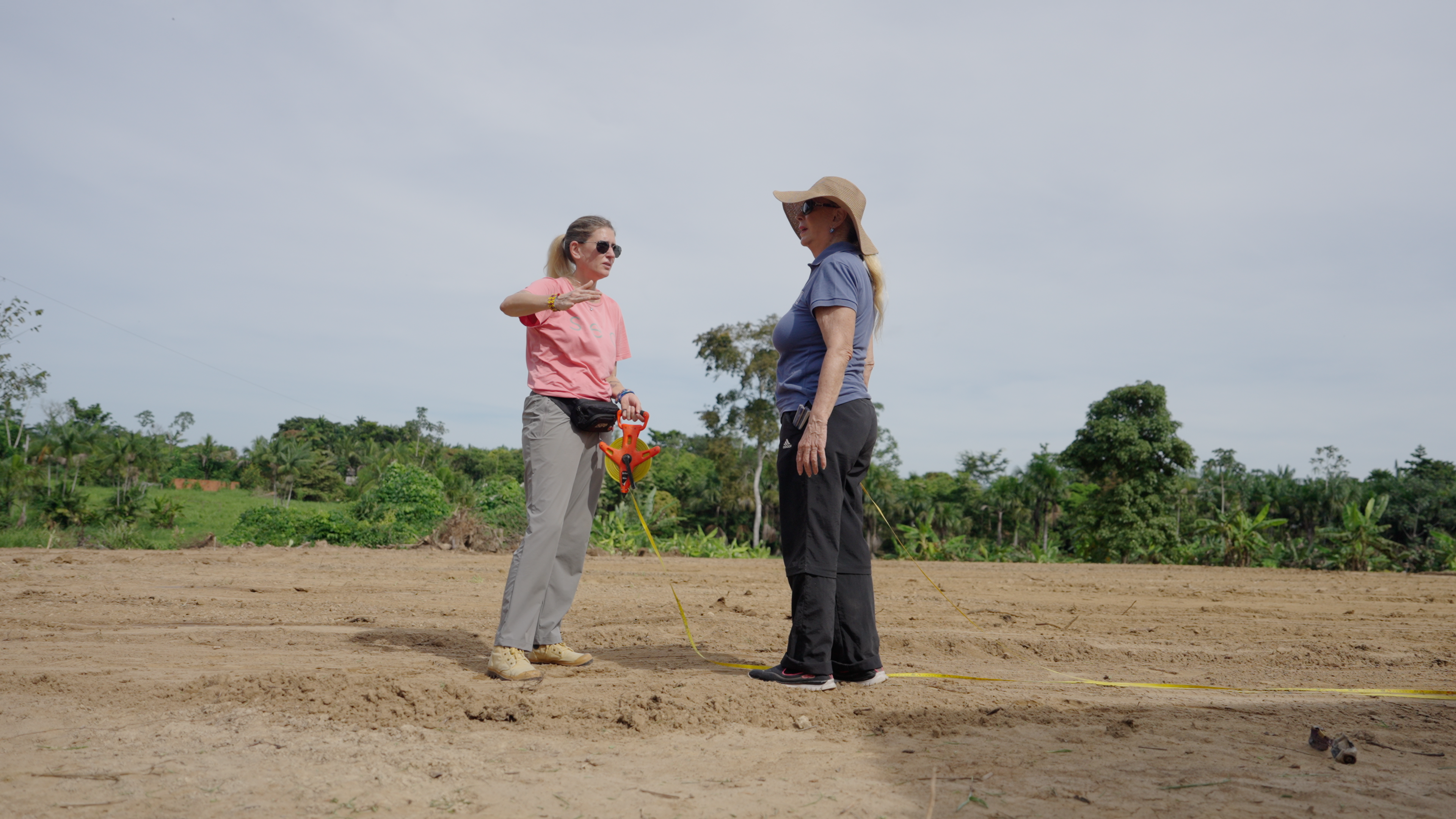 Two women measuring the field together on a cleared dirt ground