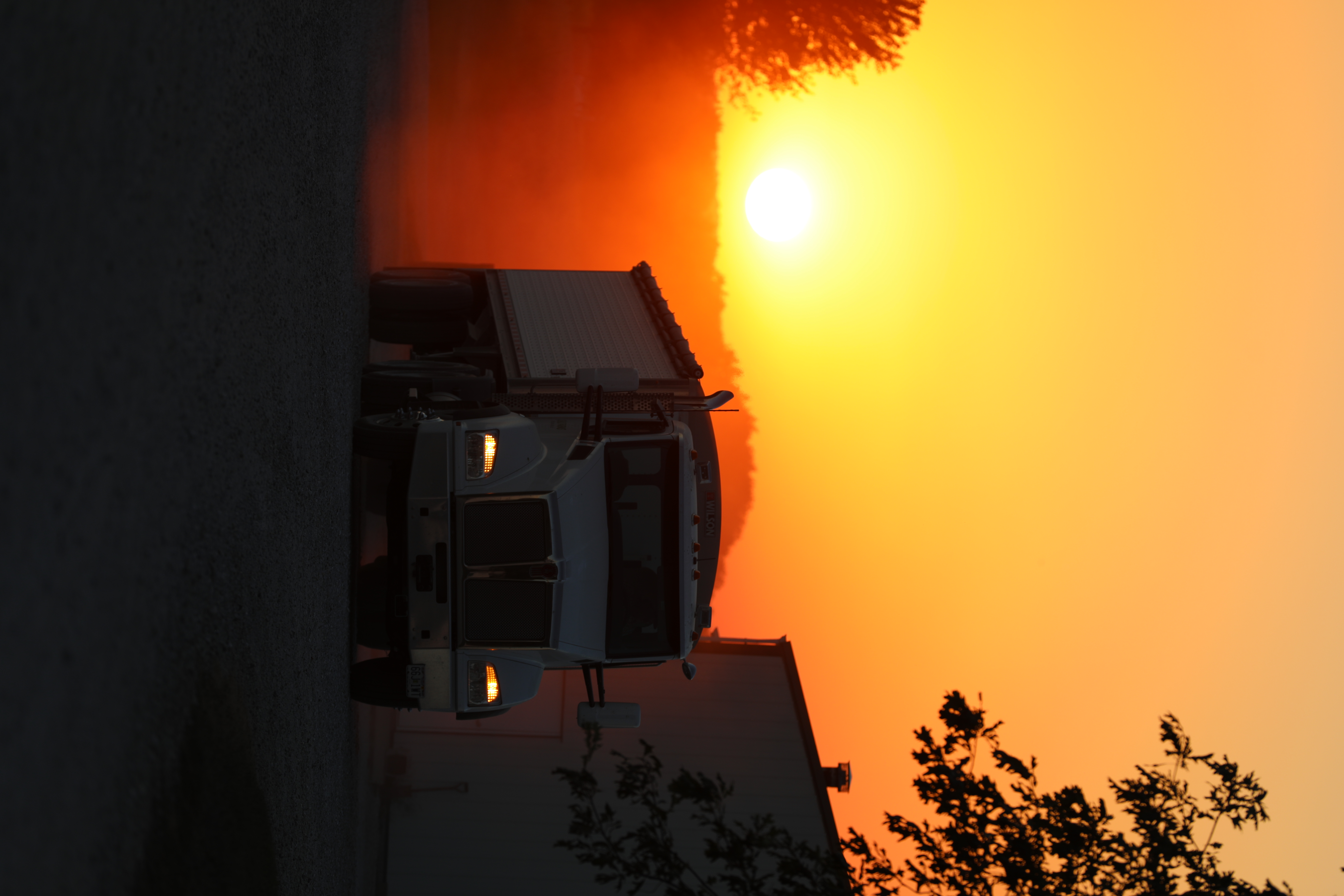 White Kenworth semi-truck silhouetted against a vibrant sunset