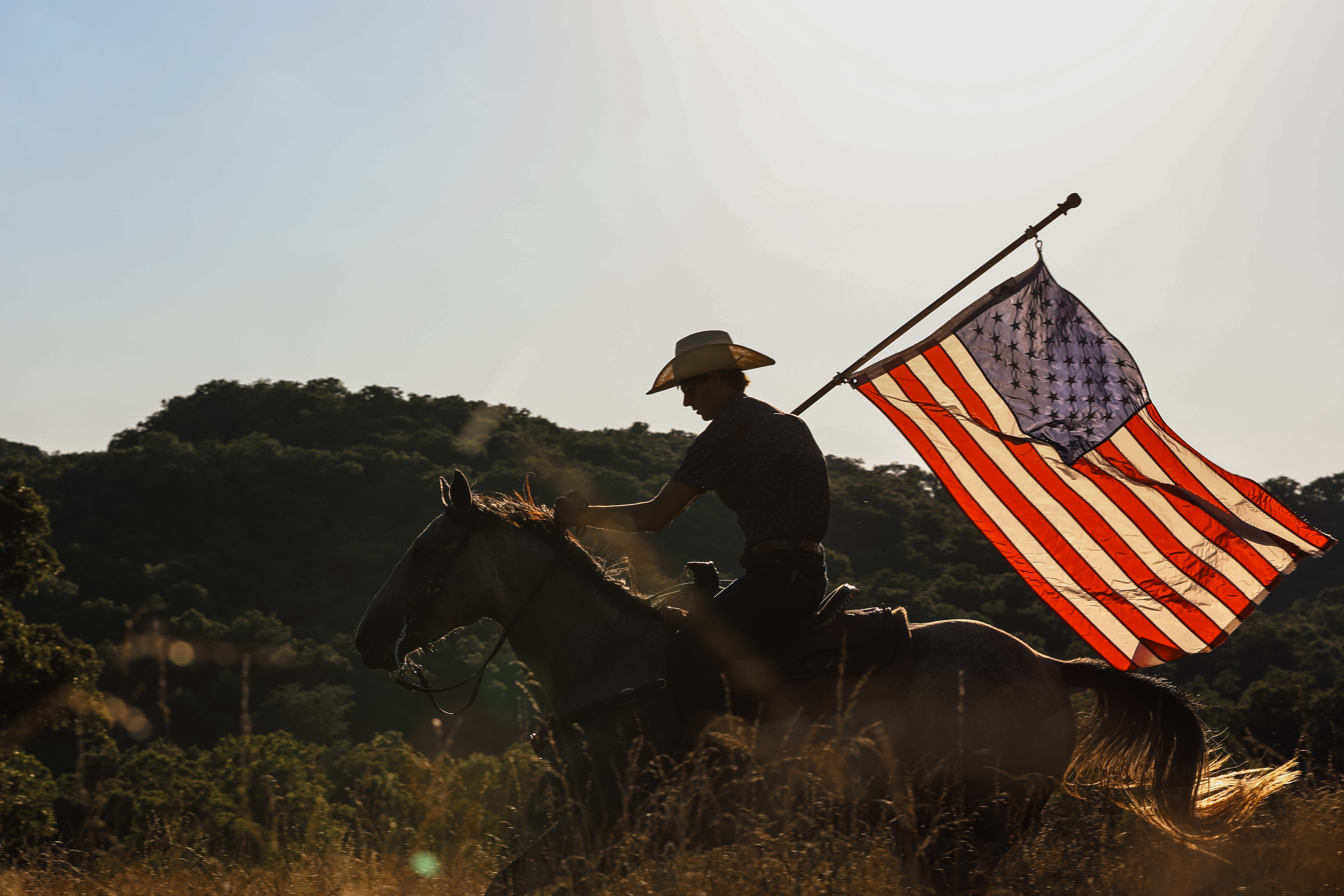 Cowboy on horseback carrying an American flag at golden hour