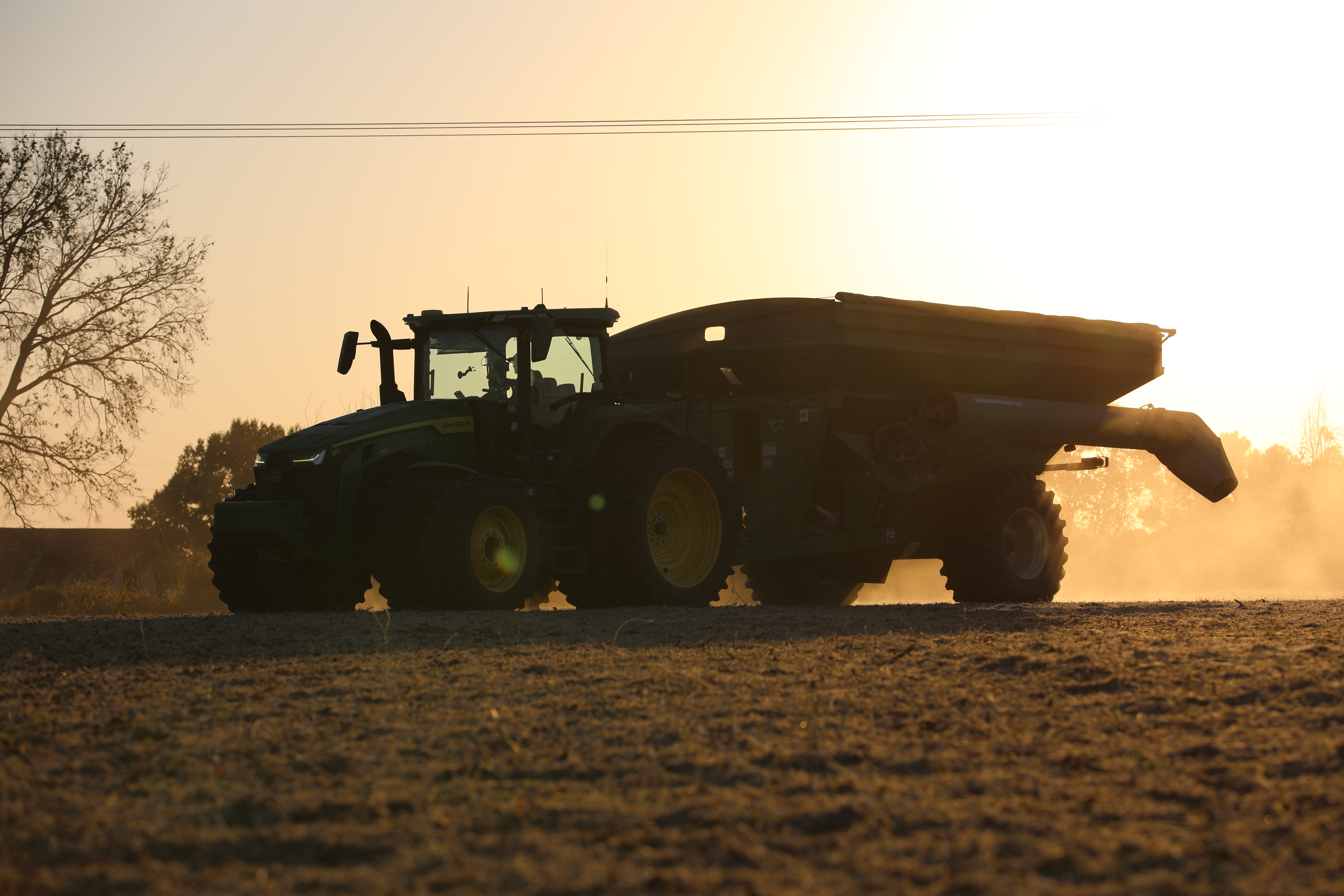 Tractor pulling a grain cart at sunset