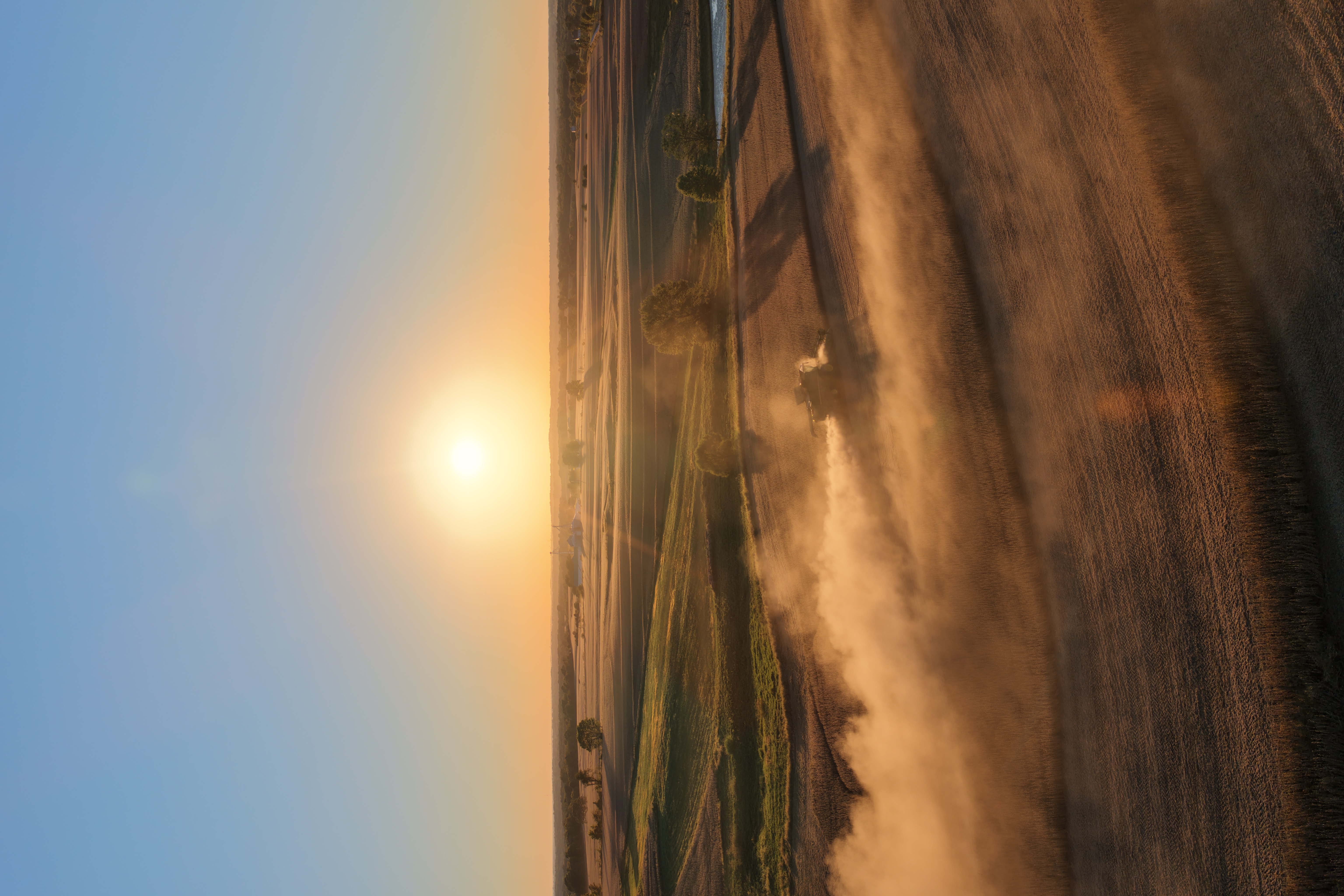 Aerial view of a combine kicking up dust at sunrise
