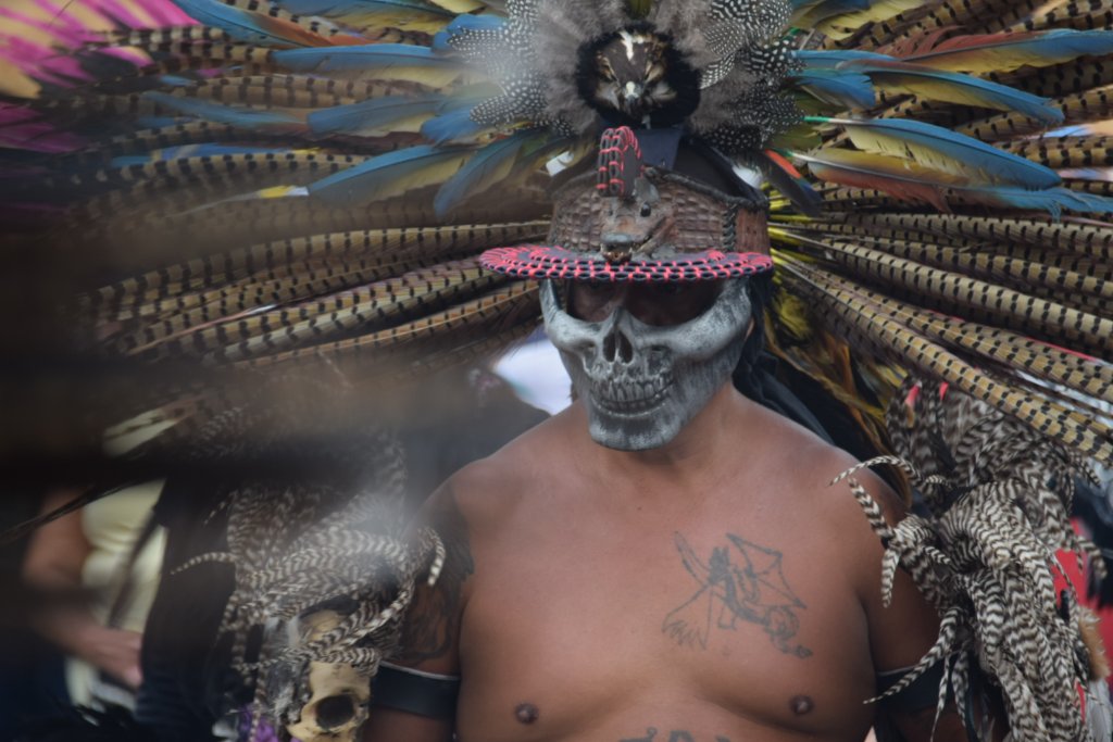 Dancer with skull mask surrounded by smoke, feathers in motion