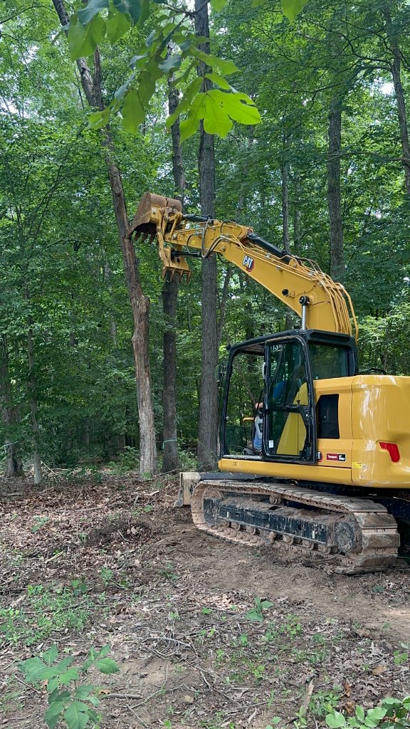 CAT 313 excavator reaching to pull and remove mature hardwood trees from wooded residential lot in Middle Tennessee — professional tree removal