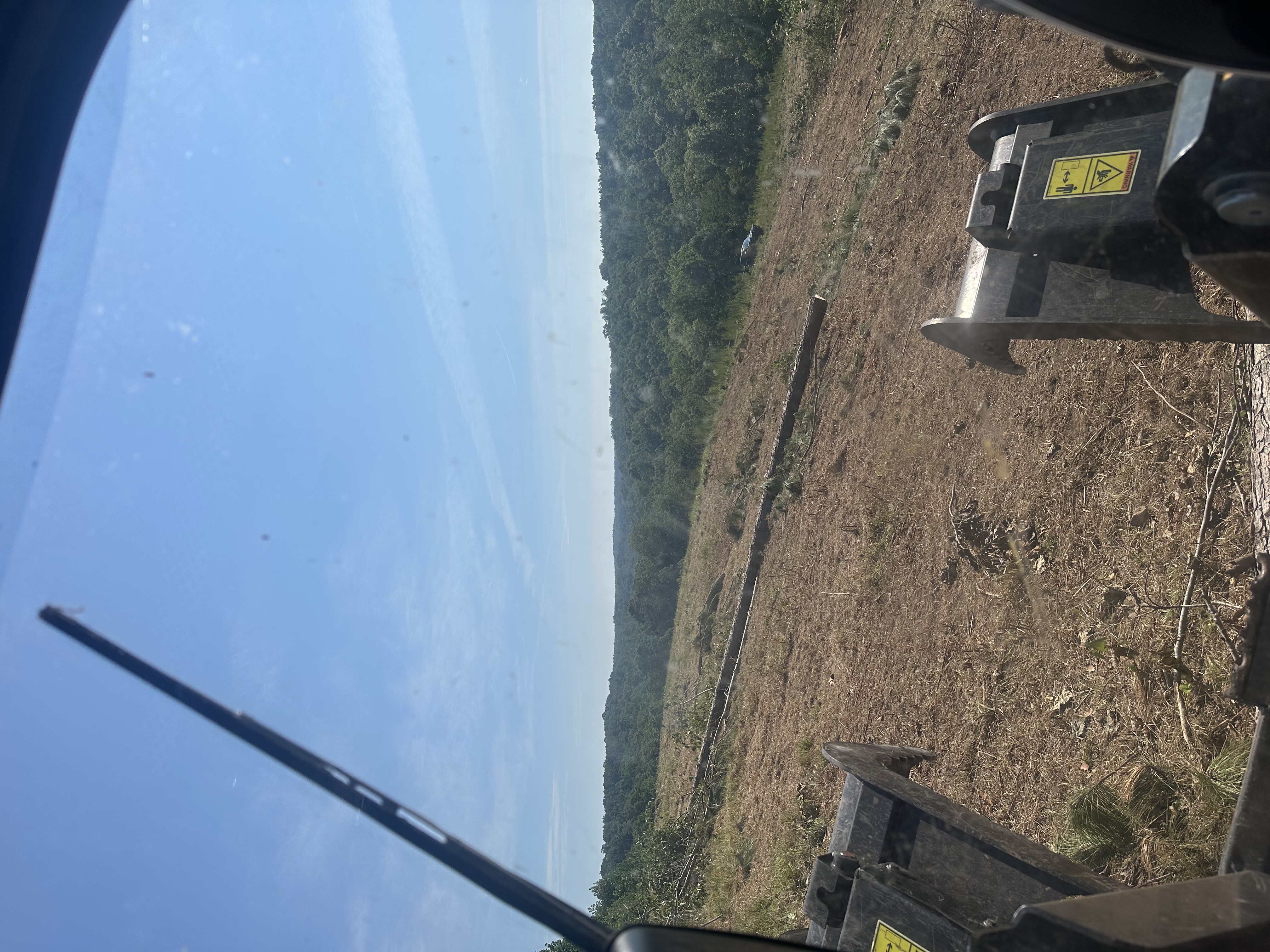 Back 40 operator cab view inside CAT track loader with grapple attachment overlooking a cleared and graded steep hillside during land clearing in Middle Tennessee