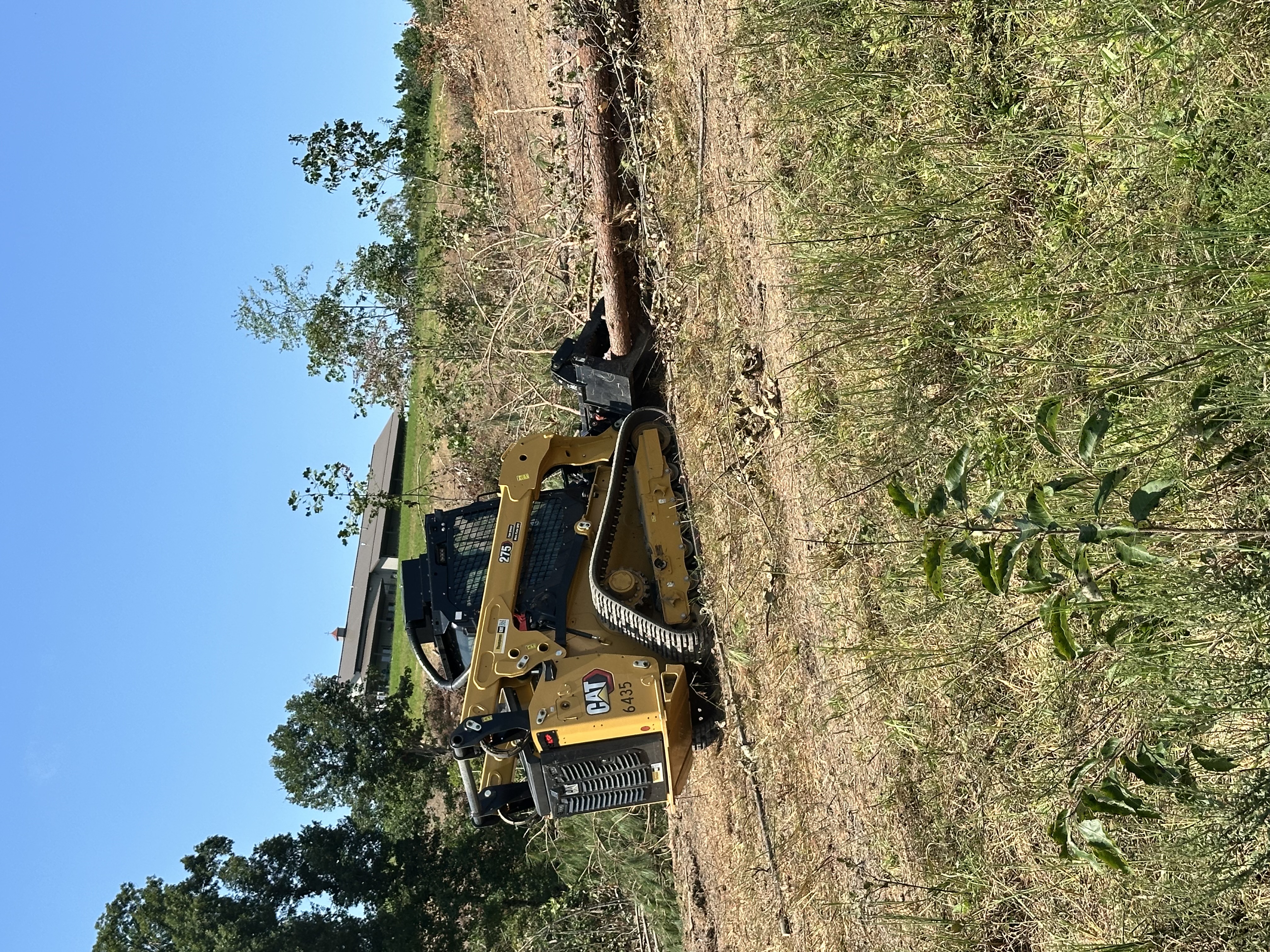 Back 40 CAT 275 skid steer with grapple bucket stacking felled logs and clearing overgrown brush during rural property site preparation in Middle Tennessee