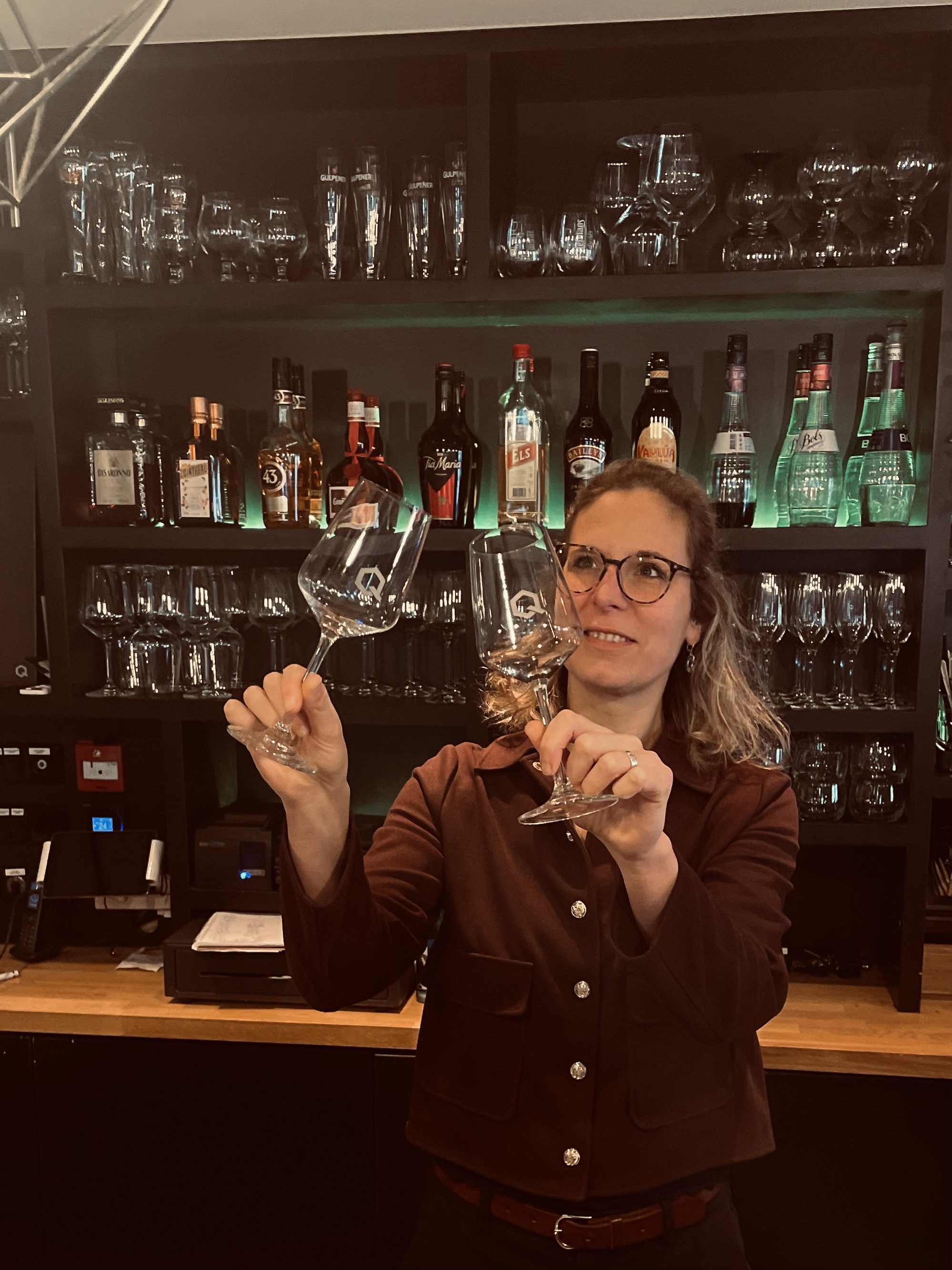 Metha van Restaurant LUQS inspecteert wijnglazen aan de bar met backlit wijnrek