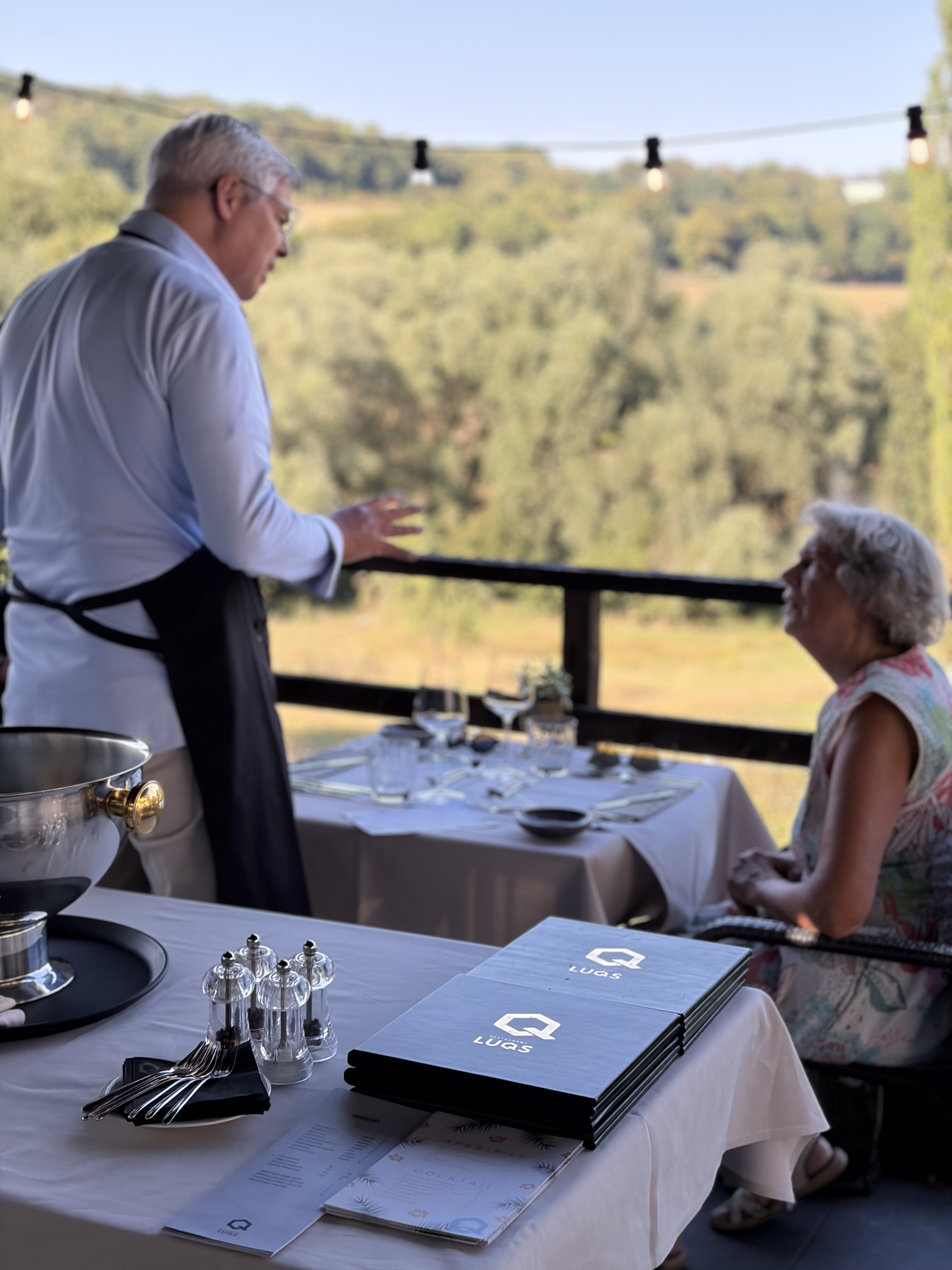 Ober legt uit aan gasten op het terras van Restaurant LUQS