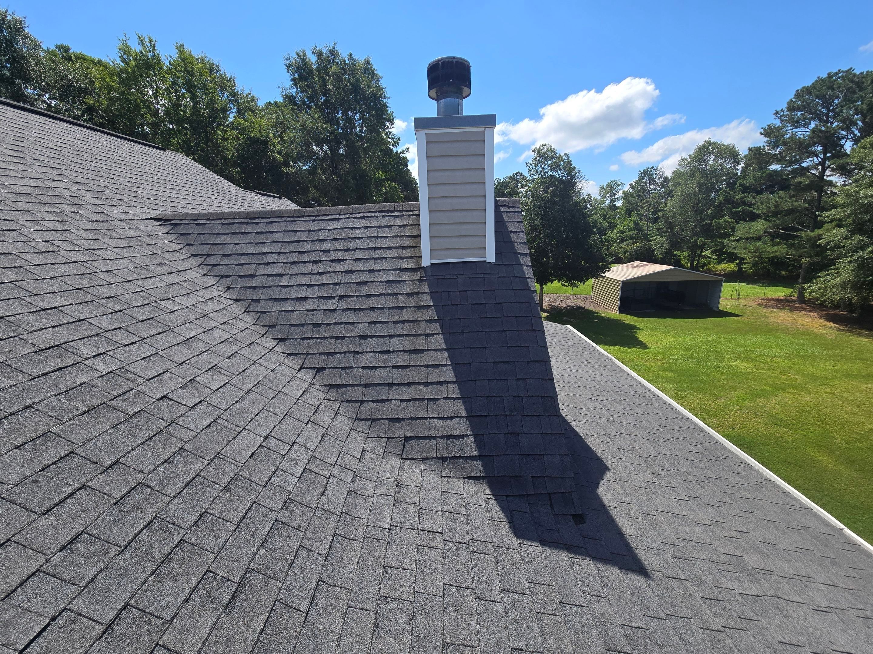 L-shaped roof section with dark gray asphalt shingles and a beige chimney before replacement