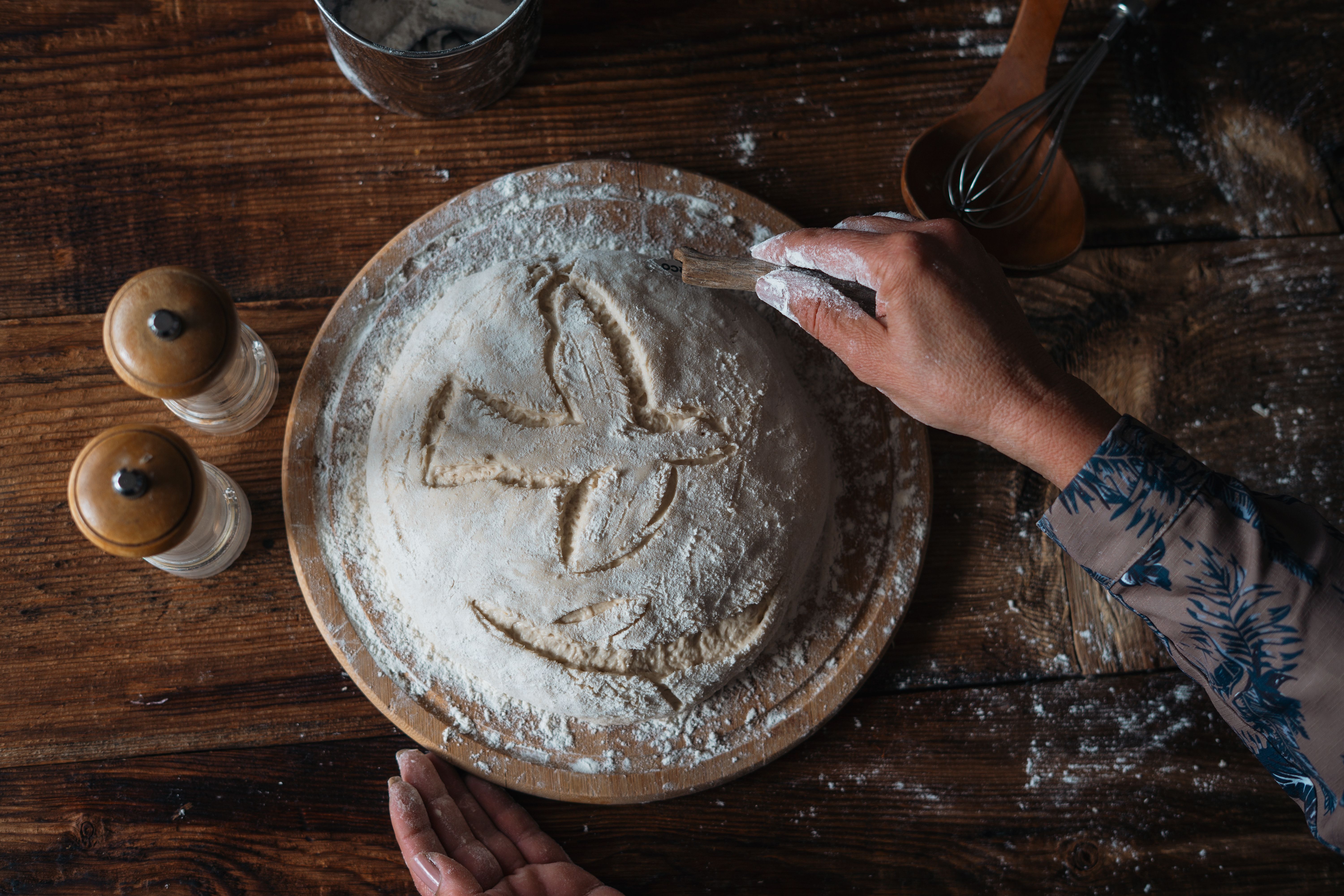 A baker scoring a decorative pattern into a round loaf of dough