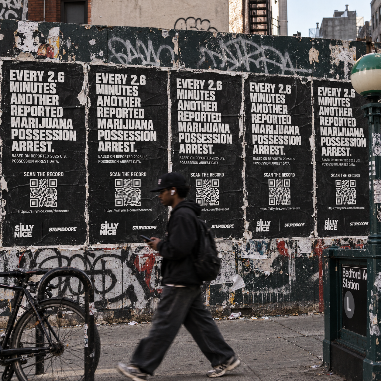Five identical THE RECORD posters tiled on a construction fence showing every 2.6 minutes another reported marijuana possession arrest, with QR codes and Silly Nice | stupidDOPE branding, near Bedford Avenue Station