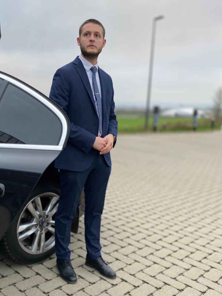 Chauffeur privé LAM Conciergerie en costume devant véhicule de prestige