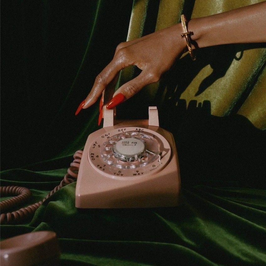 A hand lifting a vintage rotary phone receiver with soft wedding flowers in the background