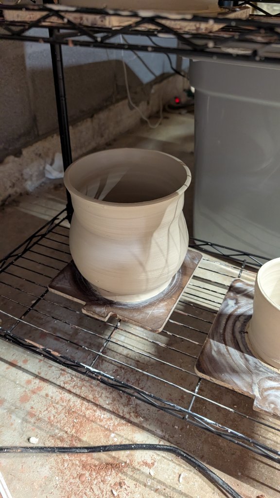 Unfired clay vase drying on studio wire rack