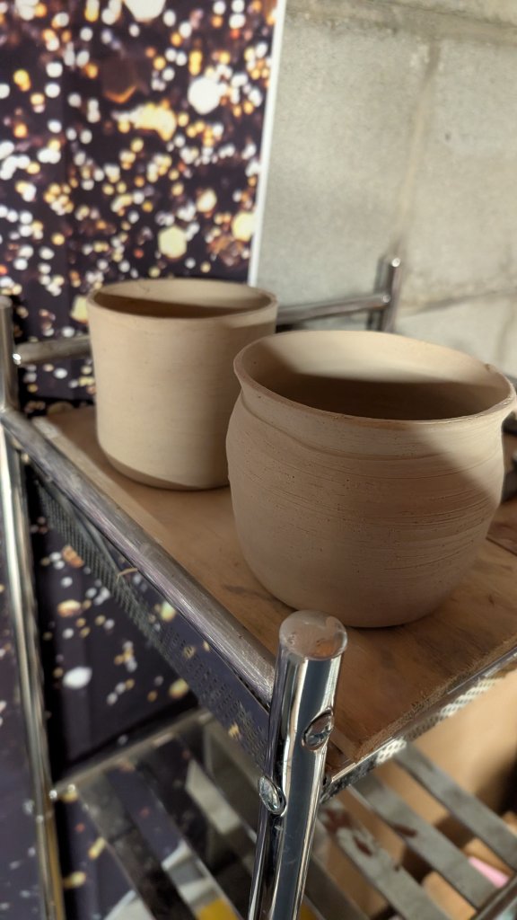Two unfired clay pots on studio shelf