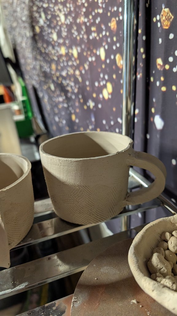 Unfired textured clay mug on rack