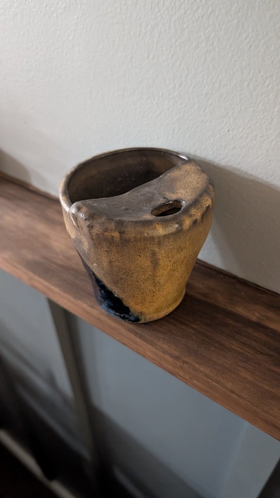 Amber and dark glazed vessel on wood shelf