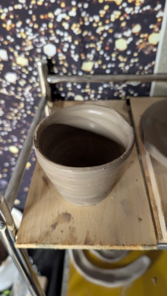 Grey clay cup drying on wood shelf