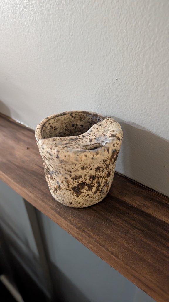 Speckled glazed ceramic vessel on wood shelf