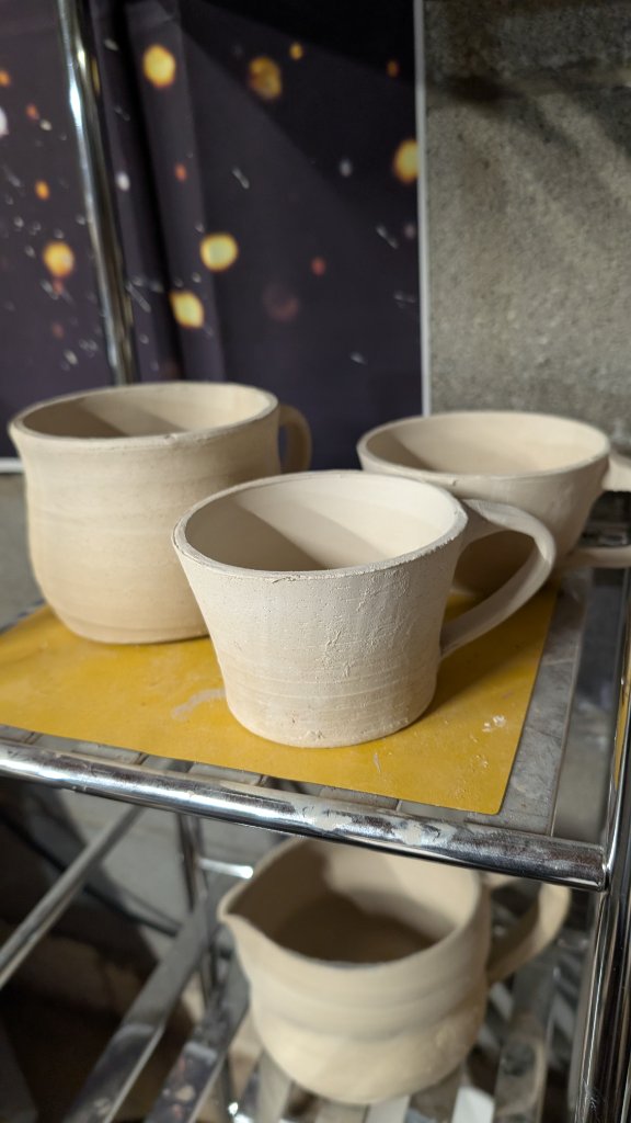 Three unfired clay mugs drying on studio rack