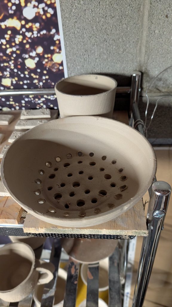 Unfired clay colander bowl on studio shelf