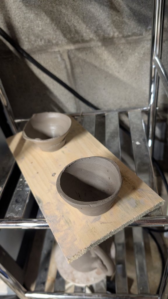 Two small pinch pot bowls drying on wood shelf