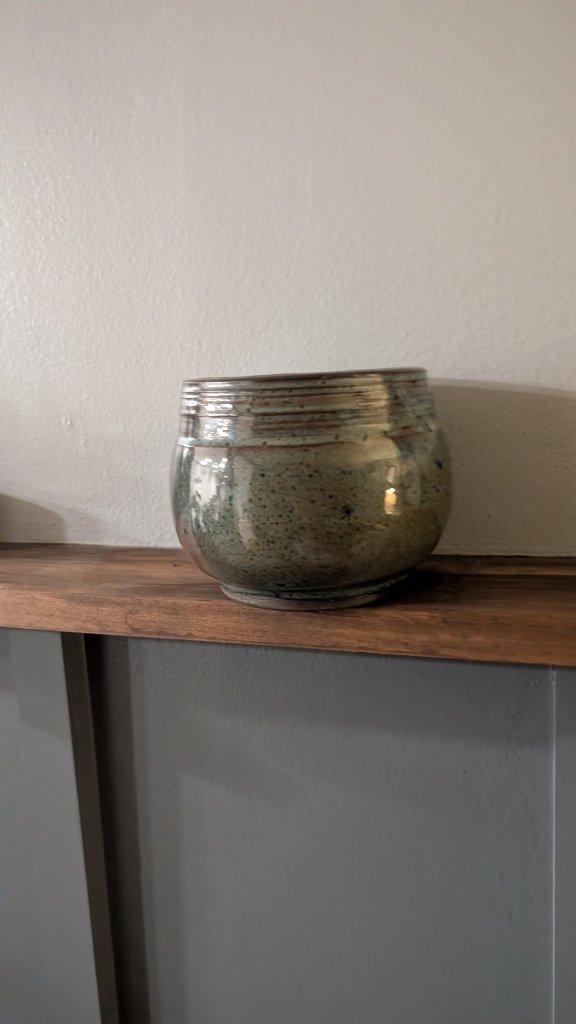 Green speckled glazed round bowl on wood shelf