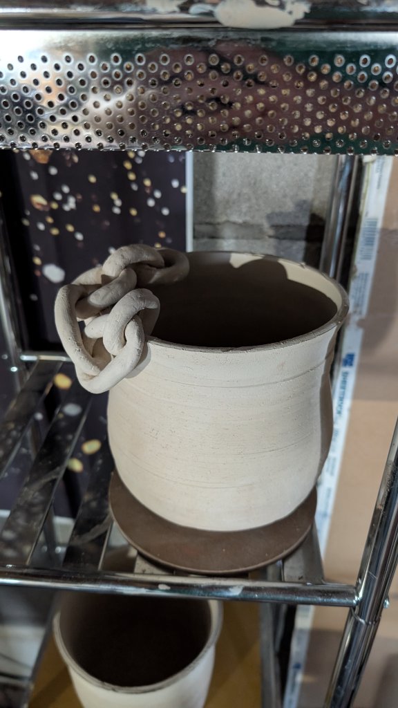 Unfired clay mug with chain handle on rack