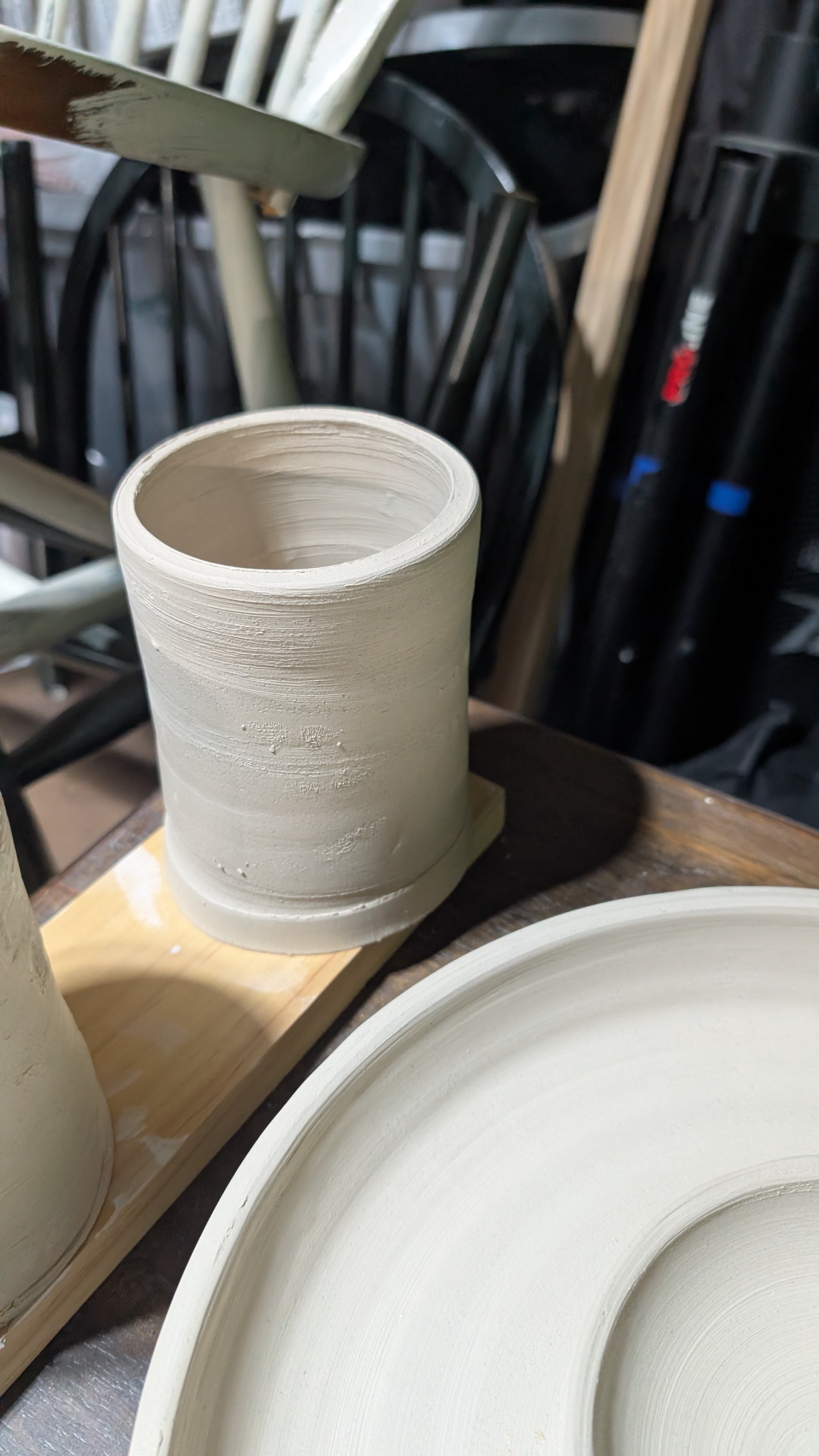 Unfired cylindrical clay mug on wooden plank