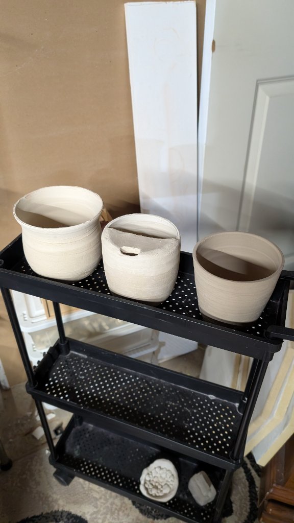 Three unfired clay pots on rolling studio cart