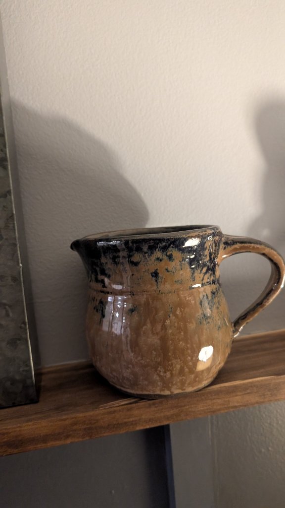 Tan and navy glazed pitcher on wood shelf