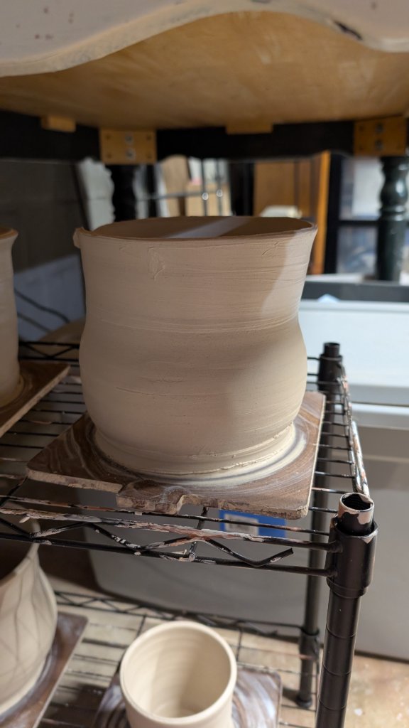 Large unfired clay vessel on drying rack