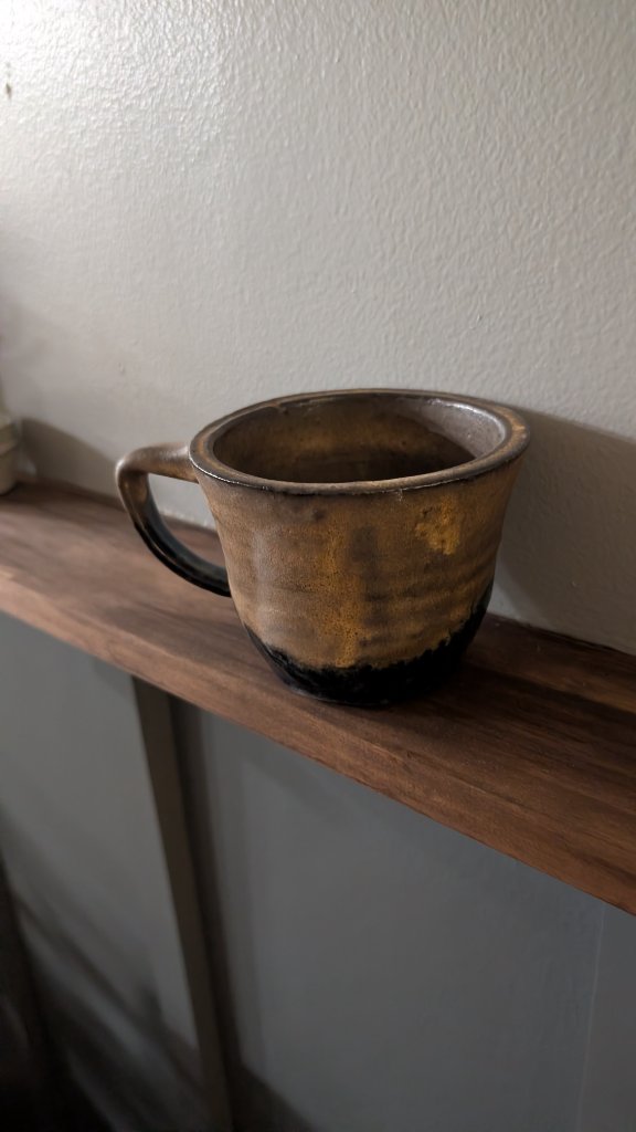 Golden brown glazed mug with handle on wood shelf