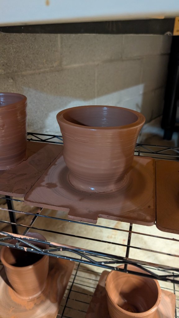 Clay cup drying on rack among other pieces