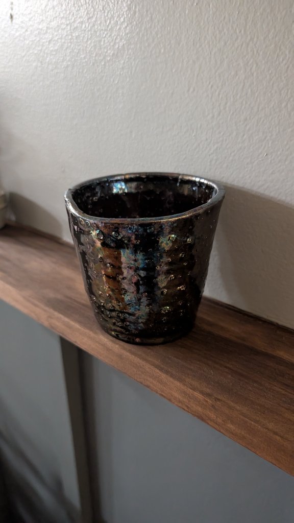 Iridescent dark glazed cup on wood shelf