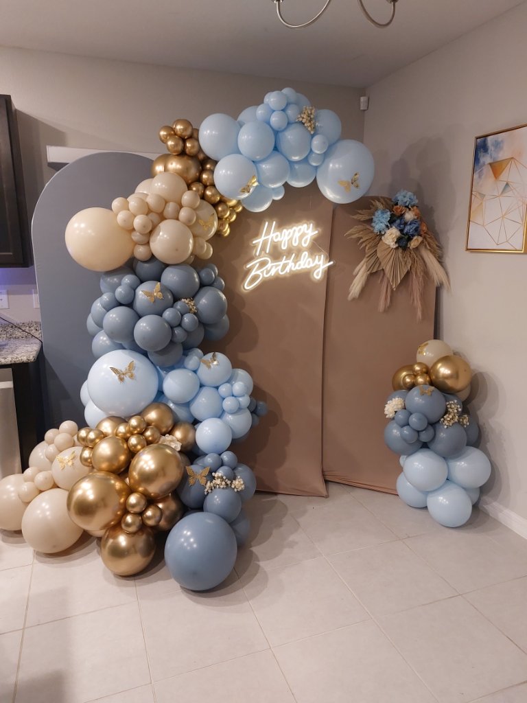 Blue and gold organic balloon garland with pampas grass accents and a Happy Birthday neon sign