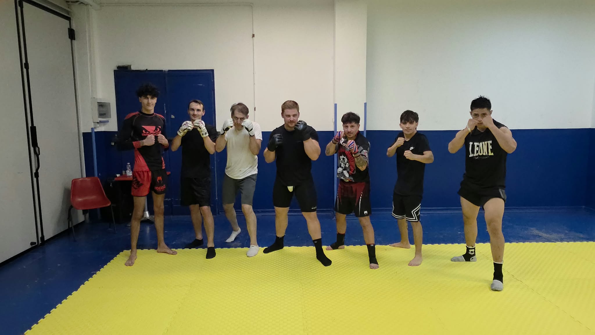 Gruppo di atleti KravMMA Extreme Torino in posa di guardia sul tatami giallo — allenamento MMA e Krav Maga