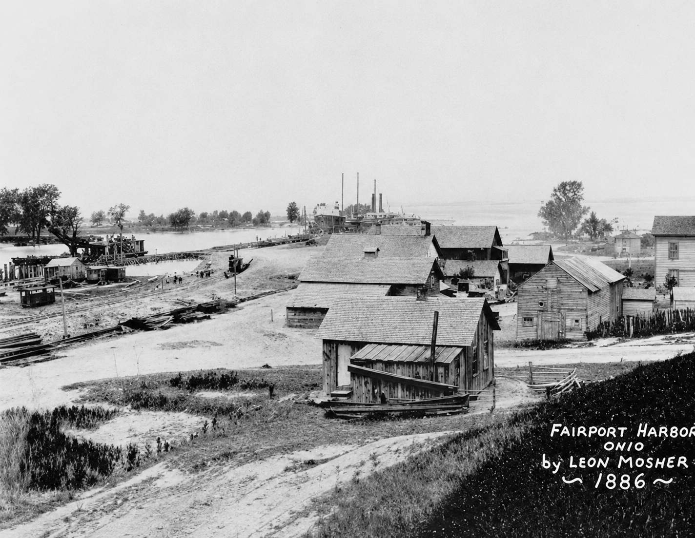 A 1886 historical photograph of Fairport Harbor, Ohio, by Leon Mosher, showing wooden buildings and a harbor scene, with a slider to toggle between the original black-and-white image and a colorized restoration.