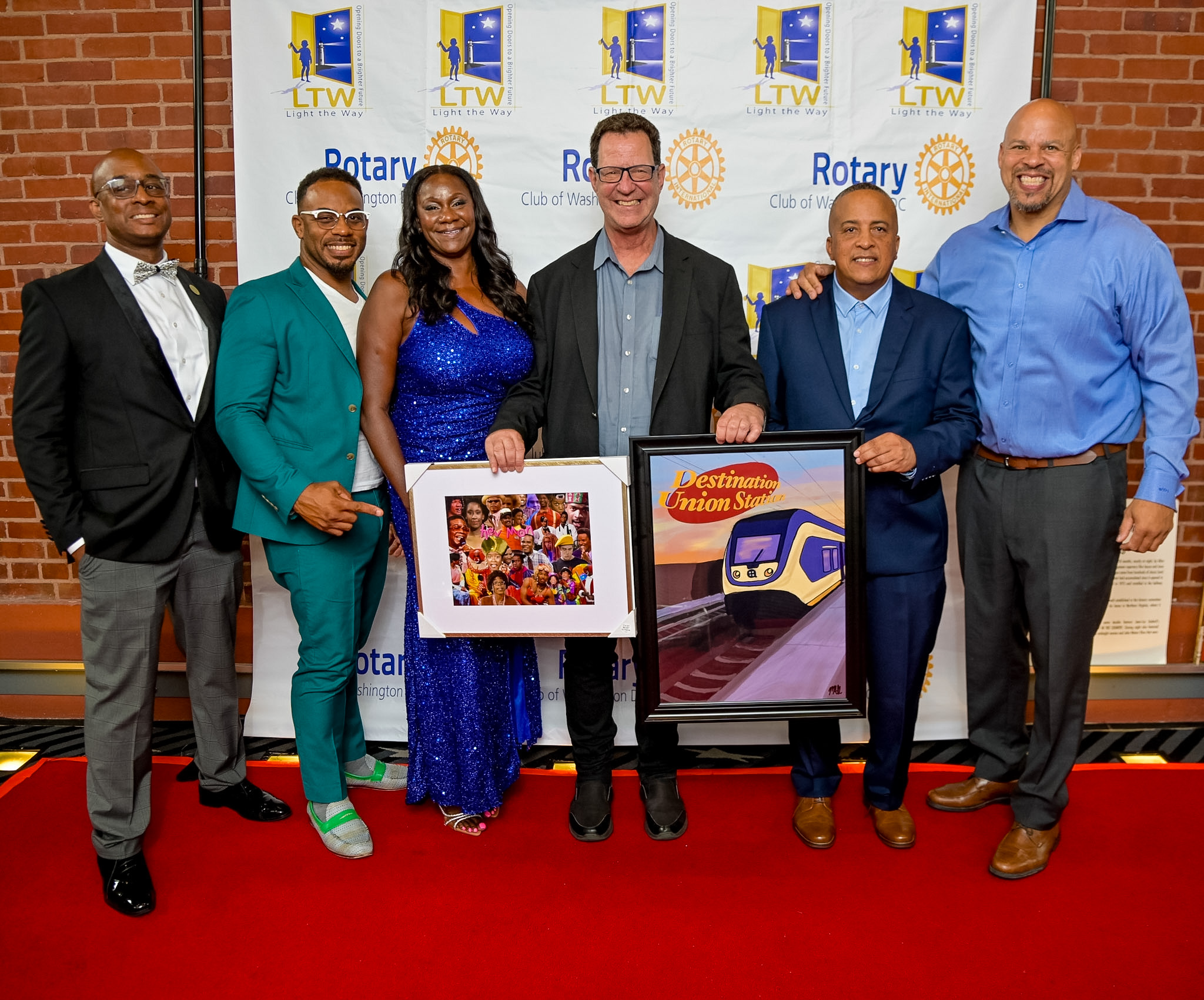 Six guests with framed artwork posing on the Red Carpet at the 2026 Premiere