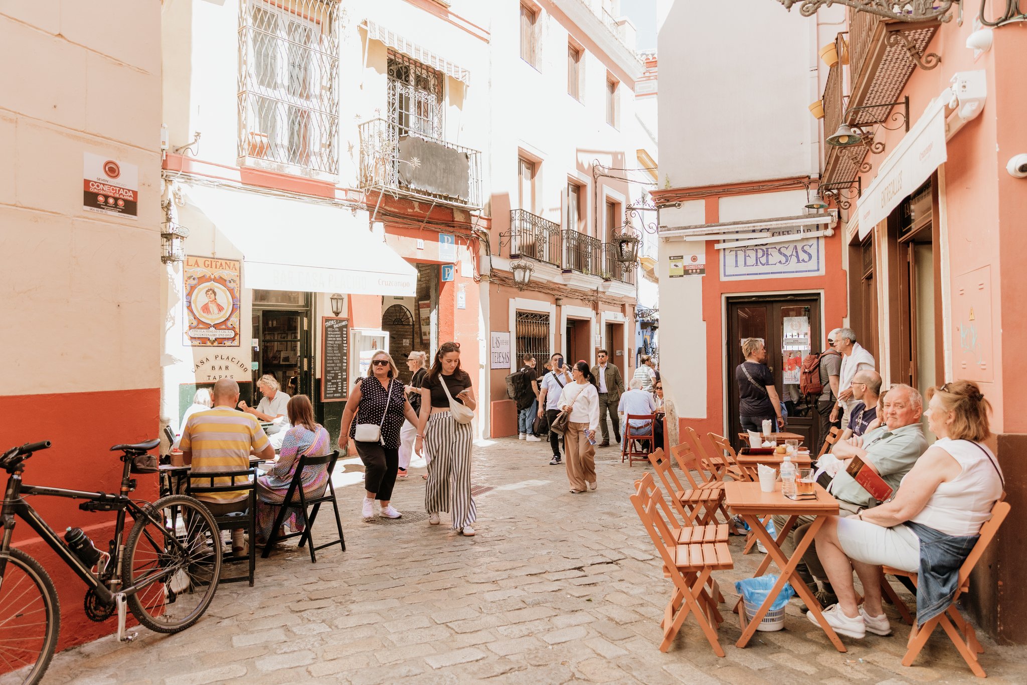 A bustling cobblestone street in Seville lined with tapas bars and café tables