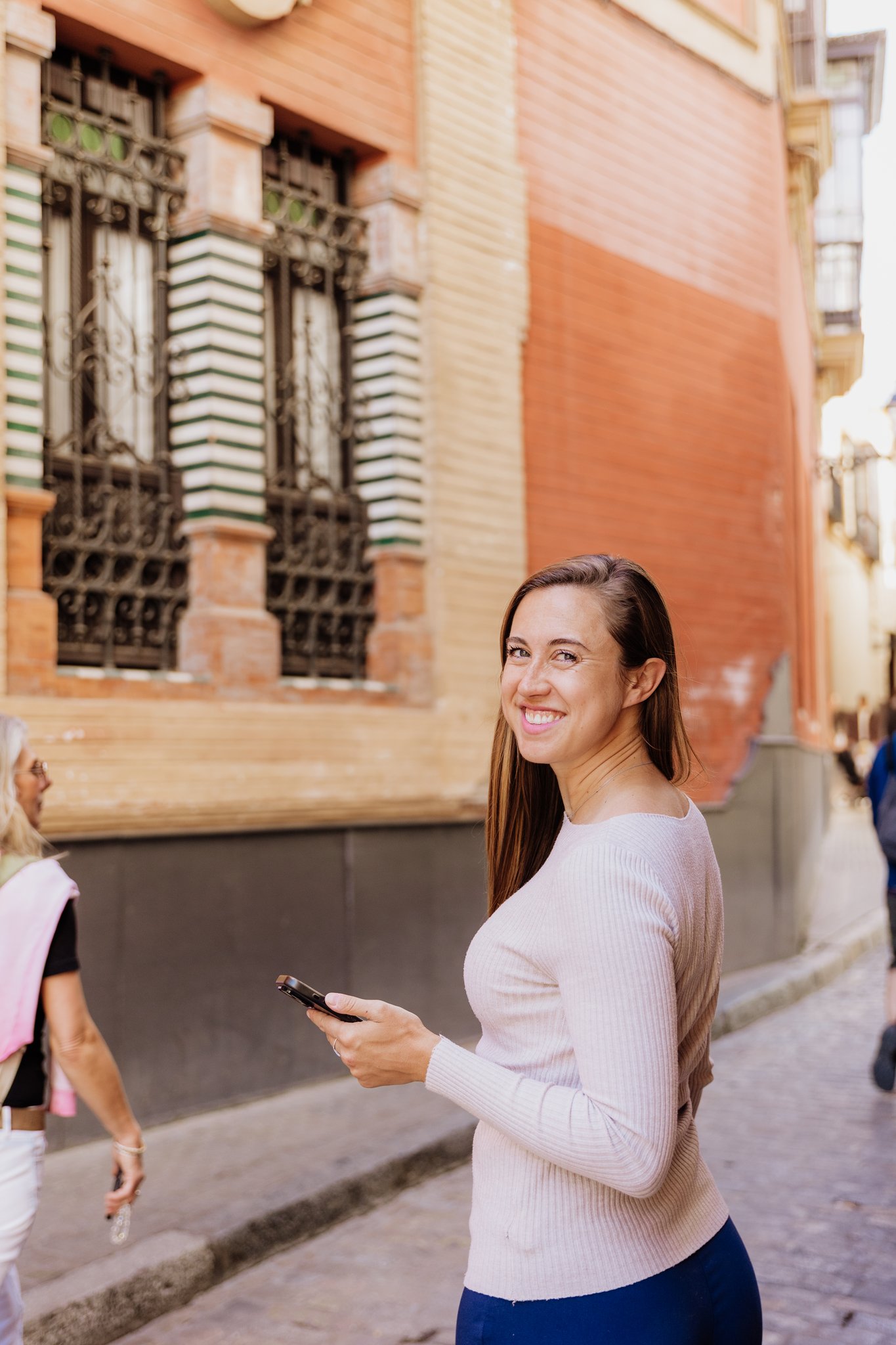 Stephanie Jahn walking down a narrow sunlit street in a historic Spanish town, smiling at the camera