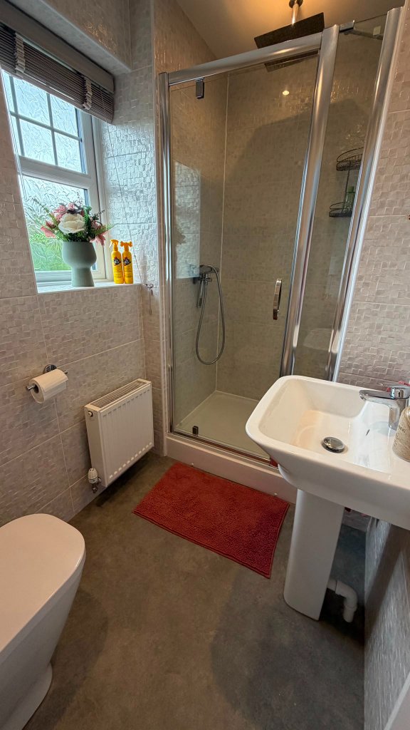 The calm spa bathroom at House of Paws Retreat — Pet Head grooming bottles on the windowsill, a walk-in glass shower and pedestal sink for a gentle wash and groom