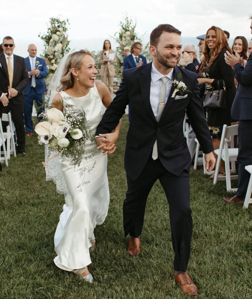 Joyful couple walking back down the aisle after ceremony with floral arch backdrop