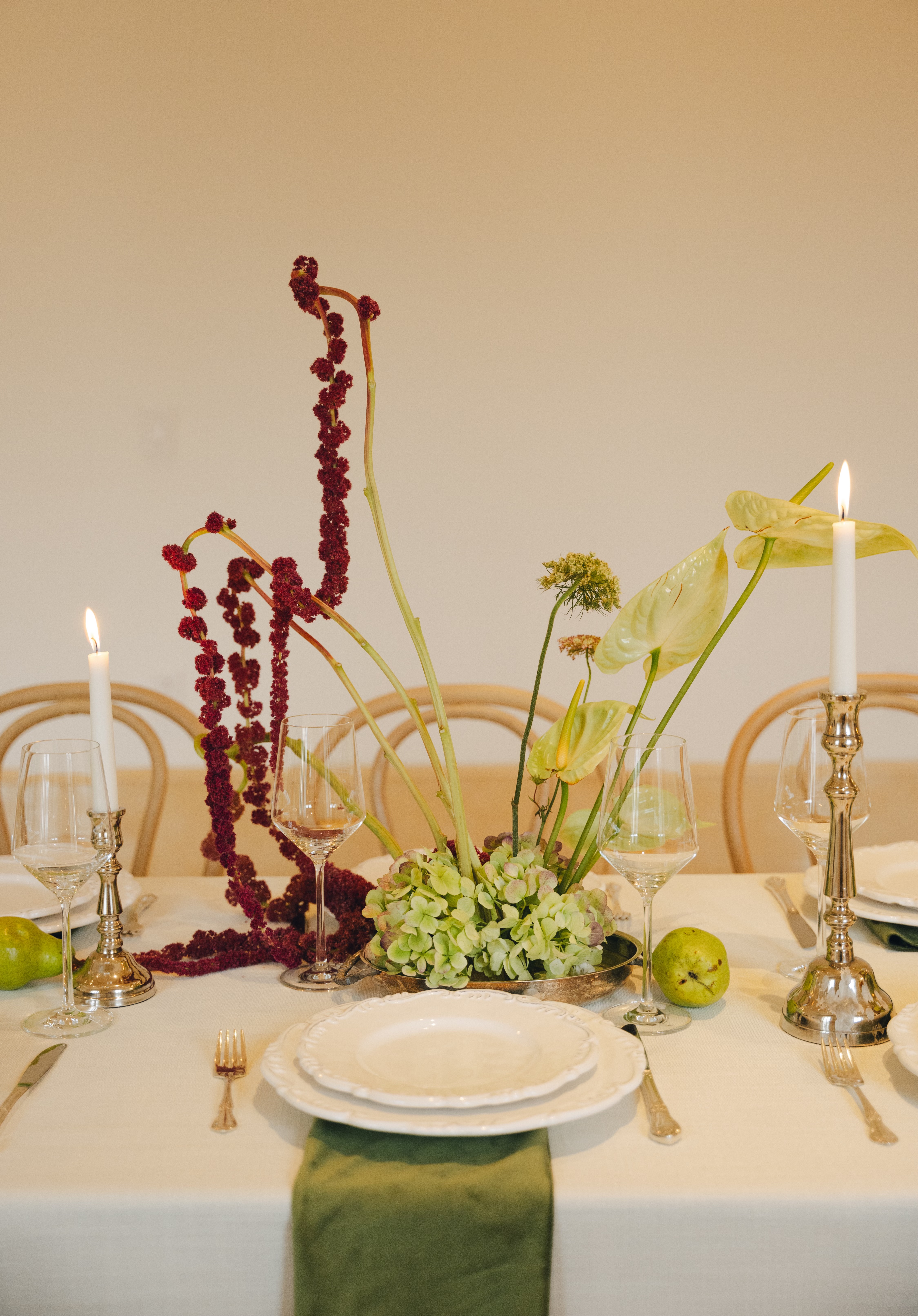 Sculptural centerpiece of burgundy amaranthus and lime anthurium with silver candlesticks on white linen