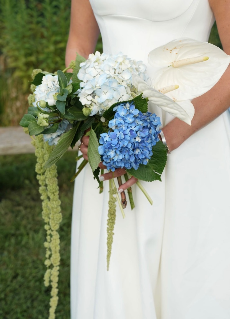 Bride holding blue hydrangea and white anthurium bouquet with trailing amaranthus