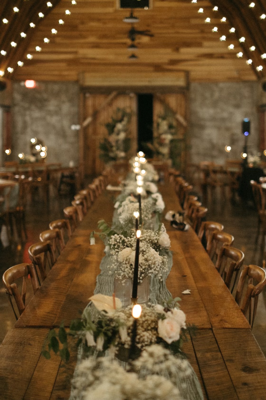 Long barn reception table with baby's breath, blush roses and black taper candles under string lights