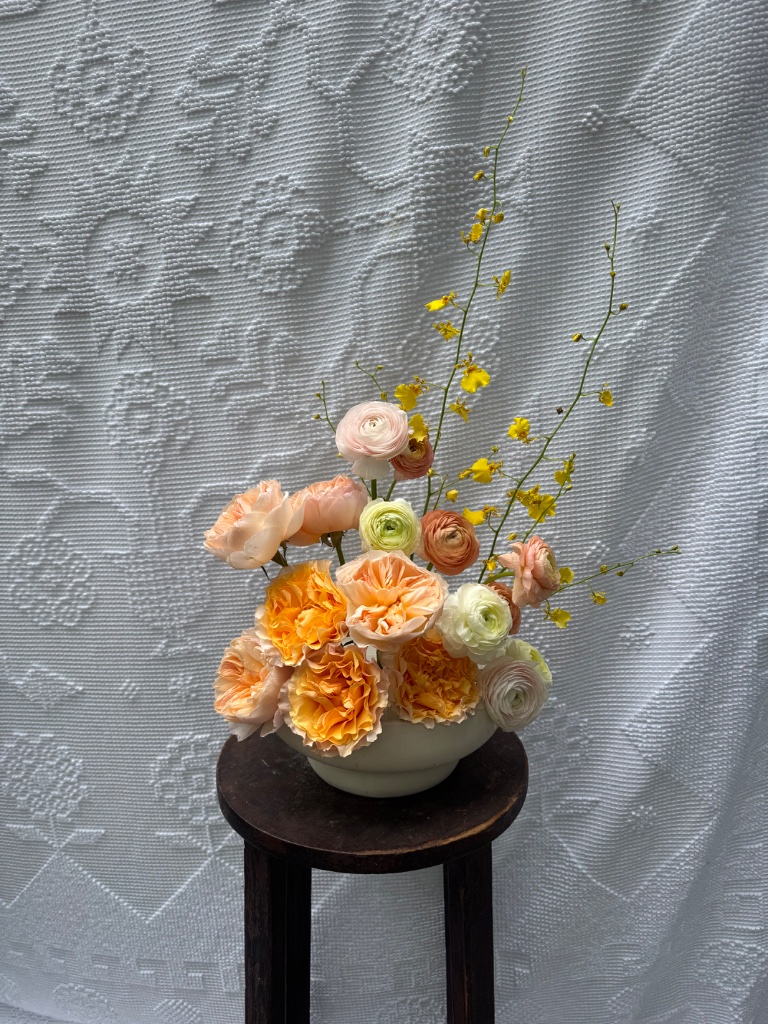 Orange and peach floral arrangement with oncidium orchids in white ceramic bowl