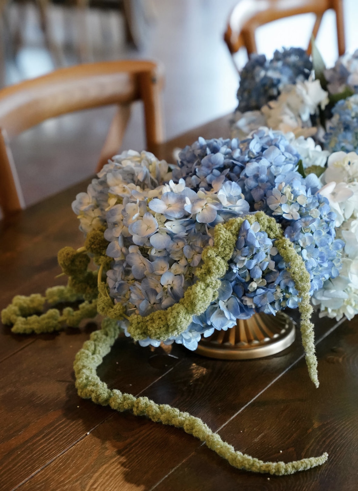 Close-up of blue hydrangea centerpiece with trailing green amaranthus in a brass bowl