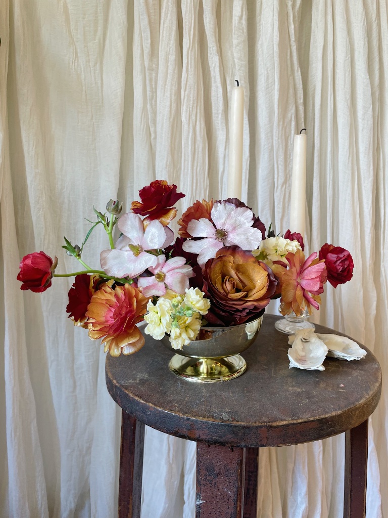 Autumn floral arrangement in brass bowl with ranunculus, cosmos and taper candles